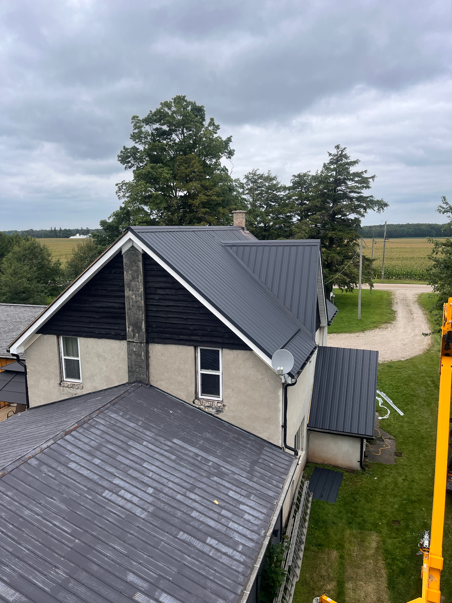 Finished dark metal roof installed on a rural farmhouse with multiple rooflines