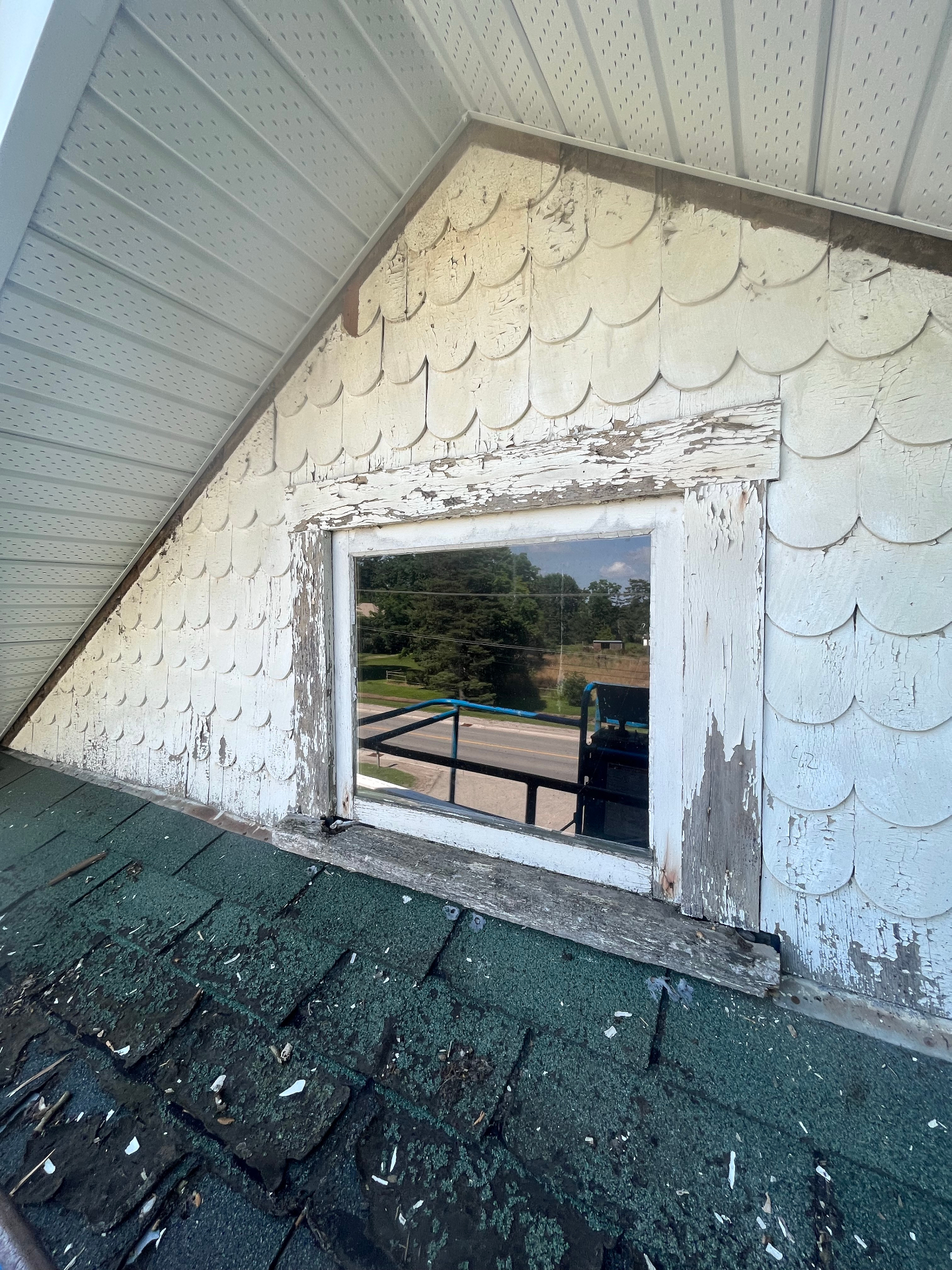 Weathered upper wall cladding and deteriorated trim around a dormer window before exterior repair