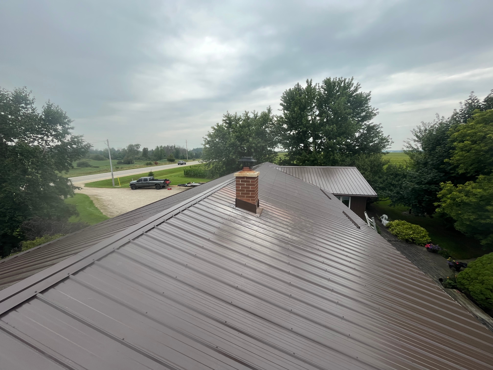 Completed brown metal roof on a rural home with clean ridge and chimney flashing details
