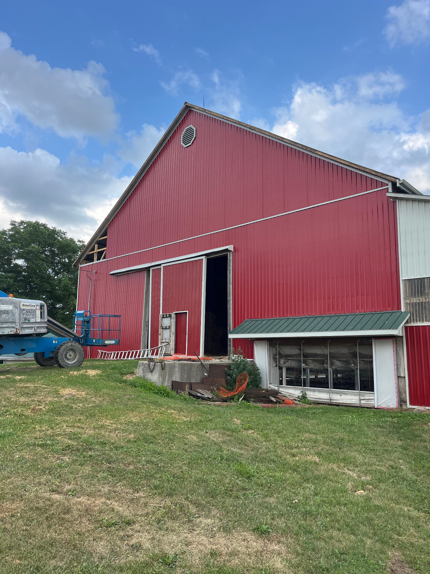 Completed red steel siding installation on a large bank barn with green metal roof accents