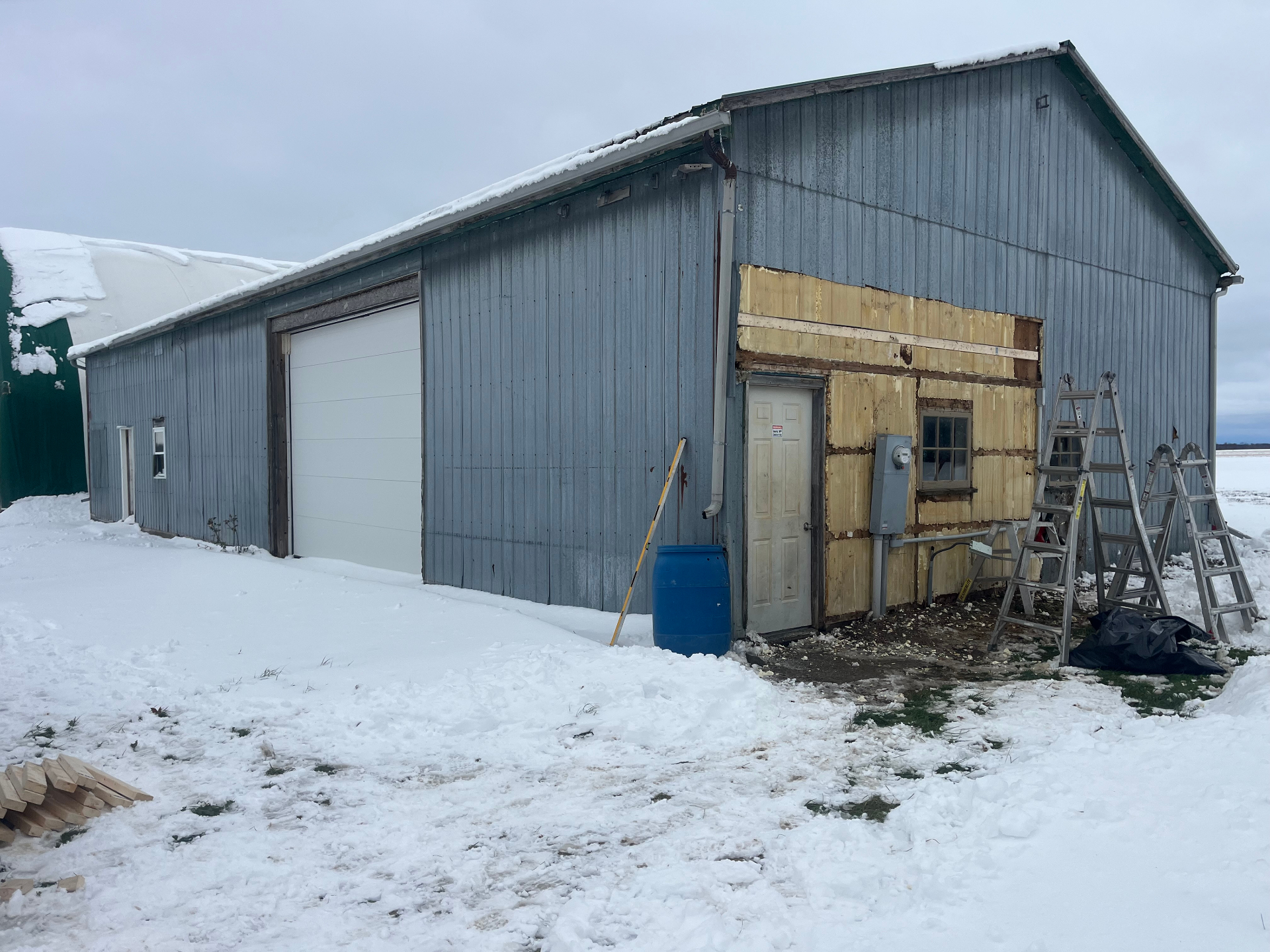 Rural farm shop with original blue steel siding partially removed in winter, ready for replacement