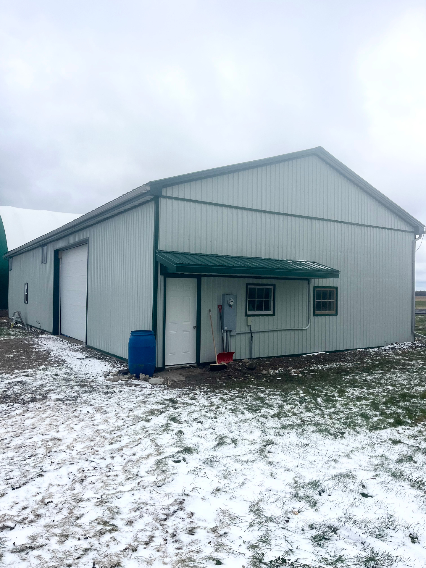 Completed white farm shop with green trim and new steel siding after exterior re-cladding