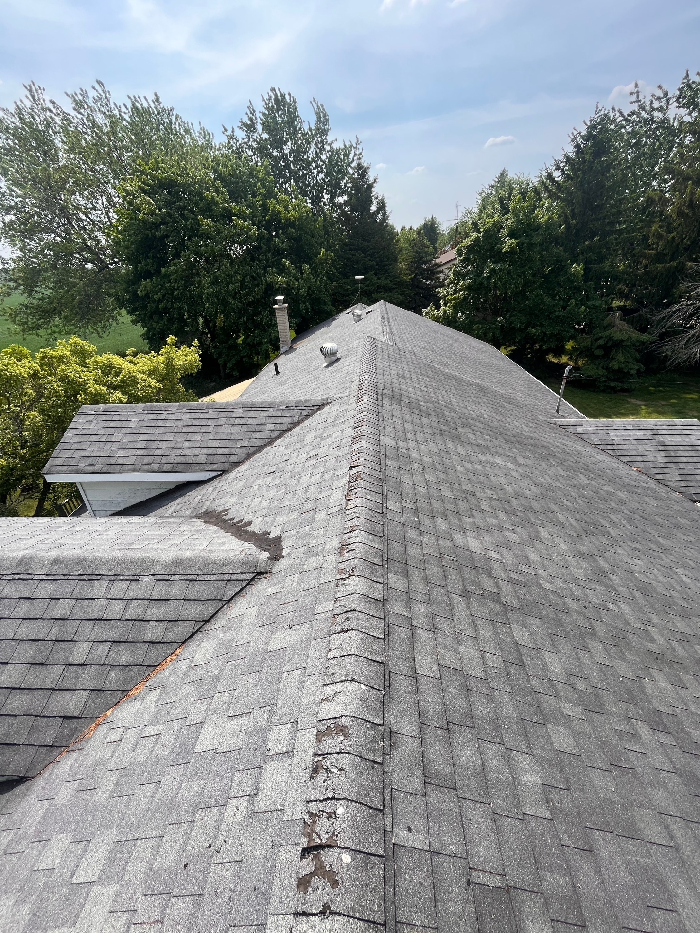 Aging asphalt shingle roof inspection showing wear and damaged ridge cap on a Huron County home